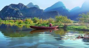 Un pequeño barco rojo en un río sereno en Vietnam, rodeado de exuberante vegetación y montañas bajo un cielo azul claro, crea una escena ideal durante el Viaje por Vietnam en 8 días. - ForTwo - Planes para parejas