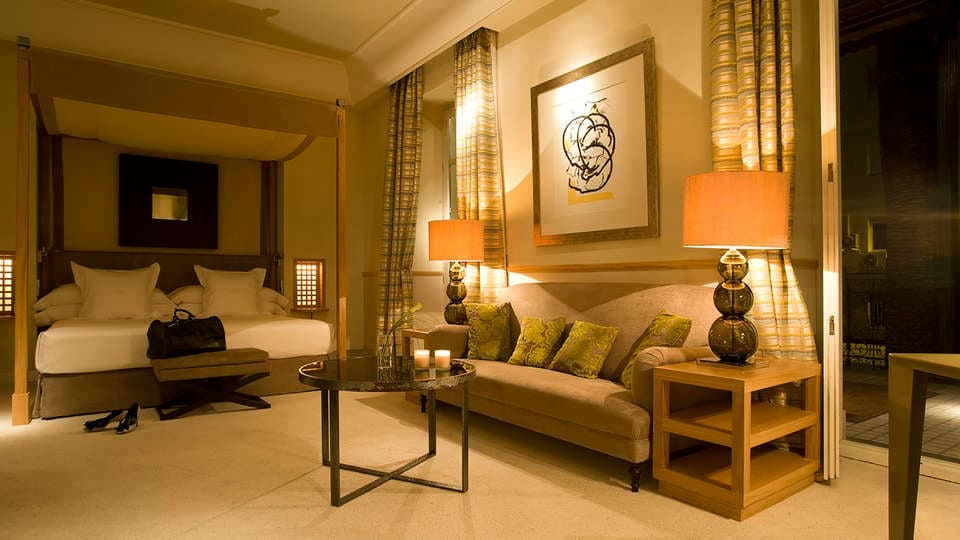 Escápese al elegante Hotel Villa Oniria—Granada, que ofrece una lujosa cama doble, un cómodo sofá, una mesa de centro de cristal con velas y paredes decoradas con obras de arte. Perfecto para el romance o la serenidad en su exquisito spa con nuestra "Escapada romántica con spa en el hotel Villa Oniria 4 estrellas". - ForTwo - Planes para parejas