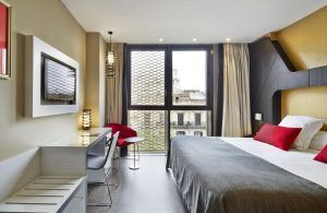 Alójese en el Hotel Vincci Gala de Barcelona, donde le espera una habitación moderna con una cama grande, una elegante decoración en rojo y gris, un televisor, un escritorio y una ventana con impresionantes vistas a la ciudad. - ForTwo - Planes para parejas