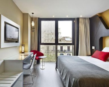 Alójese en el Hotel Vincci Gala de Barcelona, donde le espera una habitación moderna con una cama grande, una elegante decoración en rojo y gris, un televisor, un escritorio y una ventana con impresionantes vistas a la ciudad. - ForTwo - Planes para parejas