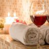 Dos copas de vino tinto y toallas enrolladas sobre una superficie de baldosas, con velas encendidas cerca, crean la magia de la vinoterapia. Disfrute de este capricho en Ambrosia Urban Spa en Barcelona. - ForTwo - Planes para parejas