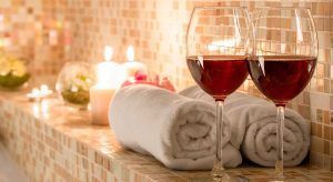 Dos copas de vino tinto y toallas enrolladas sobre una superficie de baldosas, con velas encendidas cerca, crean la magia de la vinoterapia. Disfrute de este capricho en Ambrosia Urban Spa en Barcelona. - ForTwo - Planes para parejas