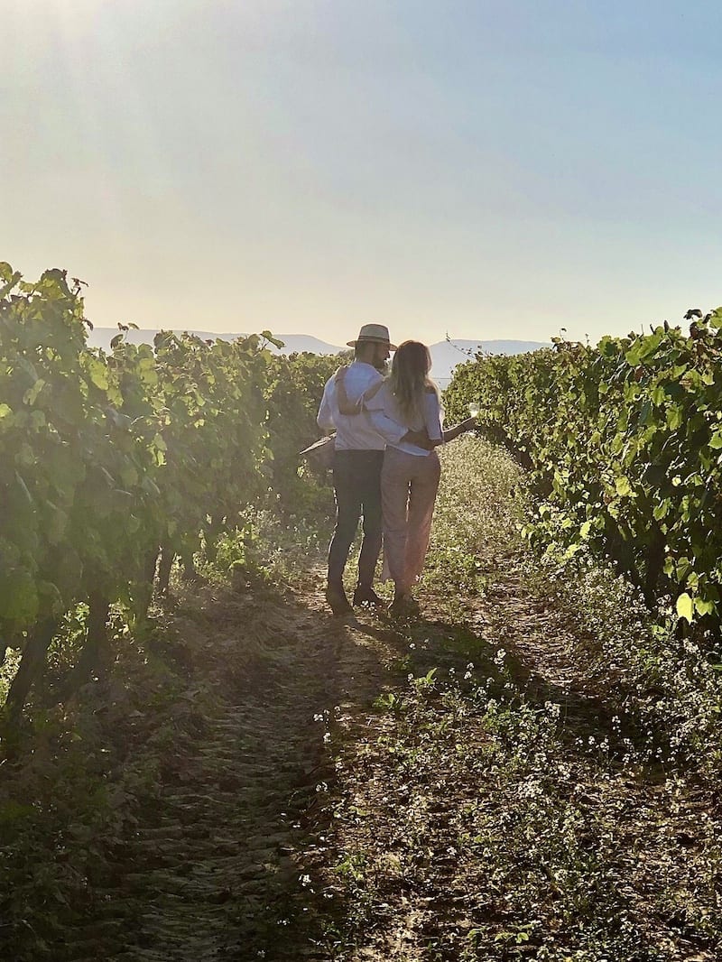 En medio de exuberantes vides verdes, una pareja disfruta de un "Día romántico de vino y gastronomía entre viñedos" en Barcelona, saboreando la promesa del viñedo iluminado por el sol de buen vino y ricos manjares. - ForTwo - Planes para parejas