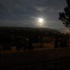 Un paisaje iluminado por la luna con árboles recortados, colinas y un tejado bajo un cielo nocturno nublado evoca el misterio de explorar el cementerio histórico de Granada durante la "Visita guiada privada al cementerio de Granada" bajo un dosel iluminado por las estrellas. - ForTwo - Planes para parejas