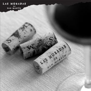 Tres corchos de vino descansan delicadamente sobre un paño blanco cerca de una elegante copa, capturando la esencia de "Cata de vino bajo las estrellas en Las Moradas de San Martín (Madrid)", un tesoro madrileño. - ForTwo - Planes para parejas