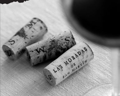 Tres corchos de vino descansan delicadamente sobre un paño blanco cerca de una elegante copa, capturando la esencia de "Cata de vino bajo las estrellas en Las Moradas de San Martín (Madrid)", un tesoro madrileño. - ForTwo - Planes para parejas