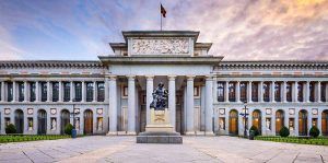 Vista frontal del Museo del Prado en Madrid, con una estatua de Velázquez al atardecer. Complemente su visita con una "Visita guiada por el Museo del Prado". - ForTwo - Planes para parejas