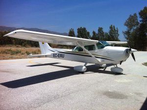 Un Vuelo en avioneta en pareja (Málaga), protagonizado por un pequeño avión blanco, está estacionado en una pista soleada con árboles y el vibrante cielo azul de Málaga de fondo. - ForTwo - Planes para parejas