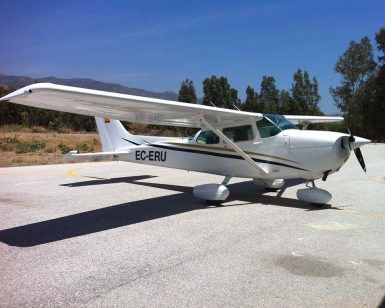 Un Vuelo en avioneta en pareja (Málaga), protagonizado por un pequeño avión blanco, está estacionado en una pista soleada con árboles y el vibrante cielo azul de Málaga de fondo. - ForTwo - Planes para parejas