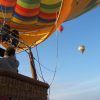 Una persona disfruta de "Un vuelo en globo privado para dos personas – Granada", con dos globos de colores bailando en el cielo despejado. - ForTwo - Planes para parejas