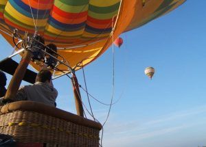 Una persona disfruta de "Un vuelo en globo privado para dos personas – Granada", con dos globos de colores bailando en el cielo despejado. - ForTwo - Planes para parejas