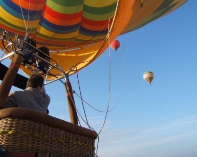 Una persona disfruta de "Un vuelo en globo privado para dos personas – Granada", con dos globos de colores bailando en el cielo despejado. - ForTwo - Planes para parejas