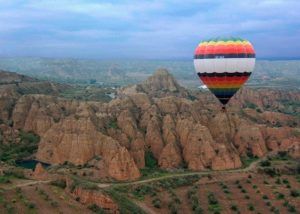 La experiencia Volar en Globo en Guadix (Granada) ofrece un colorido paseo en globo aerostático, flotando elegantemente sobre paisajes rocosos y exuberantes campos verdes bajo un cielo nublado, creando recuerdos inolvidables. - ForTwo - Planes para parejas