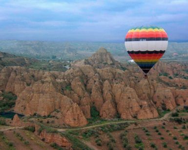 La experiencia Volar en Globo en Guadix (Granada) ofrece un colorido paseo en globo aerostático, flotando elegantemente sobre paisajes rocosos y exuberantes campos verdes bajo un cielo nublado, creando recuerdos inolvidables. - ForTwo - Planes para parejas