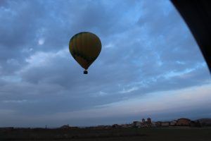 La "Oferta: vuelo en globo con hotel en Segovia" te permite sobrevolar un paisaje rural cerca de Segovia bajo un cielo nublado al atardecer, proporcionándote vistas encantadoras y momentos inolvidables. - ForTwo - Planes para parejas