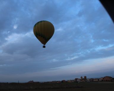 La "Oferta: vuelo en globo con hotel en Segovia" te permite sobrevolar un paisaje rural cerca de Segovia bajo un cielo nublado al atardecer, proporcionándote vistas encantadoras y momentos inolvidables. - ForTwo - Planes para parejas
