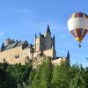 Un globo privado de "Elige un vuelo en globo privado en pareja en Madrid, Aranjuez, Segovia, Toledo y Salamanca" flota cerca de un gran castillo histórico en un día despejado, que recuerda las vistas panorámicas de Madrid. - ForTwo - Planes para parejas