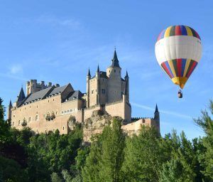 Un globo privado de "Elige un vuelo en globo privado en pareja en Madrid, Aranjuez, Segovia, Toledo y Salamanca" flota cerca de un gran castillo histórico en un día despejado, que recuerda las vistas panorámicas de Madrid. - ForTwo - Planes para parejas