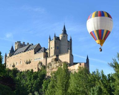Un globo privado de "Elige un vuelo en globo privado en pareja en Madrid, Aranjuez, Segovia, Toledo y Salamanca" flota cerca de un gran castillo histórico en un día despejado, que recuerda las vistas panorámicas de Madrid. - ForTwo - Planes para parejas