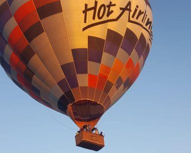 Un romántico vuelo en globo con Green Aerostacion (Sevilla) comienza contra el cielo azul claro, mostrando un colorido globo aerostático con pasajeros en la canasta. - ForTwo - Planes para parejas
