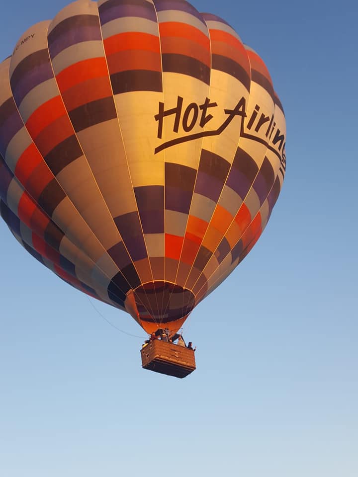Un romántico vuelo en globo con Green Aerostacion (Sevilla) comienza contra el cielo azul claro, mostrando un colorido globo aerostático con pasajeros en la canasta. - ForTwo - Planes para parejas