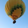 Un globo aerostático amarillo y verde flota con gracia contra el cielo despejado, invitándote a un mágico Vuelo en globo en Madrid. - ForTwo - Planes para parejas