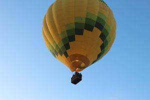 Un globo aerostático amarillo y verde flota con gracia contra el cielo despejado, invitándote a un mágico Vuelo en globo en Madrid. - ForTwo - Planes para parejas