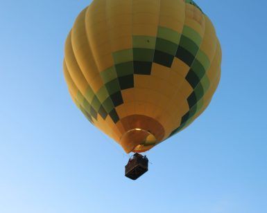 Un globo aerostático amarillo y verde flota con gracia contra el cielo despejado, invitándote a un mágico Vuelo en globo en Madrid. - ForTwo - Planes para parejas