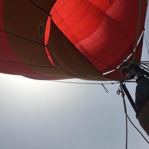 Vista desde abajo de un globo aerostático rojo y naranja, parcialmente inflado contra un cielo gris, listo para una inolvidable aventura. Una vuelta en globo con Globotur con noche en hotel (Sevilla). - ForTwo - Planes para parejas