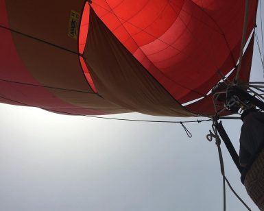 Vista desde abajo de un globo aerostático rojo y naranja, parcialmente inflado contra un cielo gris, listo para una inolvidable aventura. Una vuelta en globo con Globotur con noche en hotel (Sevilla). - ForTwo - Planes para parejas