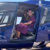 Dos personas se sientan dentro de un helicóptero azul con la puerta abierta, estacionado en una zona cubierta de hierba con vistas al impresionante paisaje durante su "Vuelo en helicóptero por la Costa del Sol (Marbella). - ForTwo - Planes para parejas