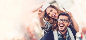 Una mujer sonriente lleva a cuestas a su pareja, ambos haciendo signos de paz para una selfie durante su Viaje sorpresa en pareja por Europa con Waynabox. - ForTwo - Planes para parejas