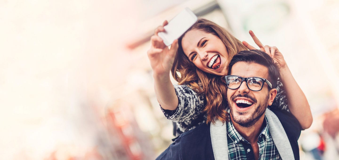 Una mujer sonriente lleva a cuestas a su pareja, ambos haciendo signos de paz para una selfie durante su Viaje sorpresa en pareja por Europa con Waynabox. - ForTwo - Planes para parejas