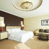 Explora la elegancia de una habitación de Hotel The Westin (Valencia), con una cama grande, pared de acento oscuro, sofá beige, mesa redonda e iluminación suave. - ForTwo - Planes para parejas