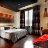 Experimente la comodidad moderna de una habitación del Wilson Boutique Hotel en Barcelona, con cama doble, silla roja, escritorio y cortinas a rayas. La cálida iluminación realza el ambiente acogedor, creando el refugio perfecto tras explorar la vibrante ciudad. - ForTwo - Planes para parejas