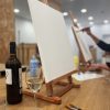 En un estudio de pintura, un lienzo en blanco reposa sobre un caballete junto a una botella de vino y una copa. - ForTwo - Planes para parejas