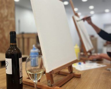 En un estudio de pintura, un lienzo en blanco reposa sobre un caballete junto a una botella de vino y una copa. - ForTwo - Planes para parejas