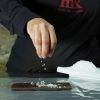 Una persona espolvorea sal sobre un bloque de chocolate rectangular sobre una superficie de aluminio, abrazando verdaderamente la esencia de "Descubre la Xocoexperience en el Museu de la Xocolata y podréis convertiros en maestros del chocolate. - ForTwo - Planes para parejas
