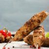 Las brochetas a la parrilla del Restaurante Libanés Yabisah en Ibiza se presentan bellamente dispuestas en una mesa, acompañadas de tomates cherry, lechuga crujiente y granos de pimienta esparcidos. - ForTwo - Planes para parejas