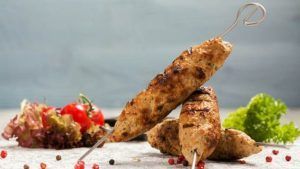 Las brochetas a la parrilla del Restaurante Libanés Yabisah en Ibiza se presentan bellamente dispuestas en una mesa, acompañadas de tomates cherry, lechuga crujiente y granos de pimienta esparcidos. - ForTwo - Planes para parejas