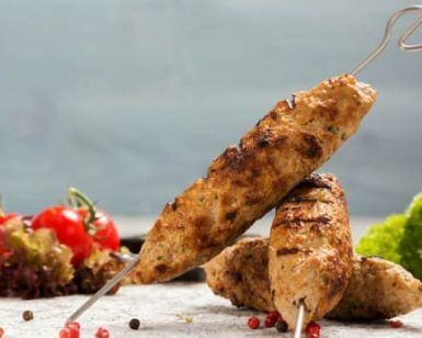 Las brochetas a la parrilla del Restaurante Libanés Yabisah en Ibiza se presentan bellamente dispuestas en una mesa, acompañadas de tomates cherry, lechuga crujiente y granos de pimienta esparcidos. - ForTwo - Planes para parejas