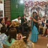 En una sala pequeña y abarrotada, una mujer con un vestido azul interpreta apasionadamente flamenco para un público embelesado, que recuerda al cautivador Espectáculo de flamenco en la Zambra María la Canastera. - ForTwo - Planes para parejas