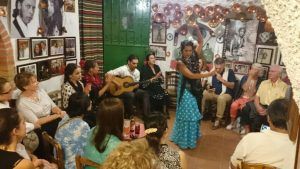 En una sala pequeña y abarrotada, una mujer con un vestido azul interpreta apasionadamente flamenco para un público embelesado, que recuerda al cautivador Espectáculo de flamenco en la Zambra María la Canastera. - ForTwo - Planes para parejas