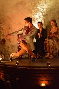 En un espacio oscuro de El Templo del Flamenco, una bailarina con traje actúa mientras dos mujeres sentadas aplauden, creando una experiencia inolvidable de Espectáculo + Menú tapeo. - ForTwo - Planes para parejas