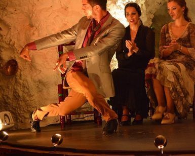 En un espacio oscuro de El Templo del Flamenco, una bailarina con traje actúa mientras dos mujeres sentadas aplauden, creando una experiencia inolvidable de Espectáculo + Menú tapeo. - ForTwo - Planes para parejas