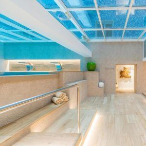 Disfrute de la lujosa piscina cubierta del Sallés Hotel Pere IV, con suelos de madera, un impresionante techo de cristal y toallas. Disfrute del Circuito de Spa + Menú Saludable en el Sallés Hotel Pere IV (Barcelona) mientras admira la exquisita decoración de la pared. - ForTwo - Planes para parejas