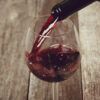 La esencia de "Cata de Vinos en Summun Gastroteca: Un Viaje Sensorial por Vinos Nacionales e Internacionales" se captura cuando el vino tinto se vierte elegantemente en una copa sobre una mesa rústica de madera. - ForTwo - Planes para parejas