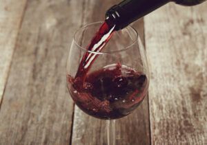 La esencia de "Cata de Vinos en Summun Gastroteca: Un Viaje Sensorial por Vinos Nacionales e Internacionales" se captura cuando el vino tinto se vierte elegantemente en una copa sobre una mesa rústica de madera. - ForTwo - Planes para parejas