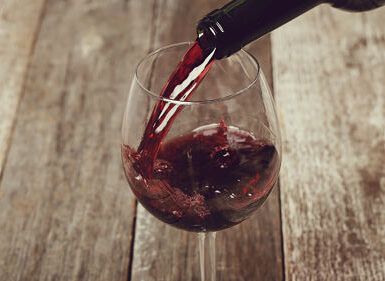 La esencia de "Cata de Vinos en Summun Gastroteca: Un Viaje Sensorial por Vinos Nacionales e Internacionales" se captura cuando el vino tinto se vierte elegantemente en una copa sobre una mesa rústica de madera. - ForTwo - Planes para parejas