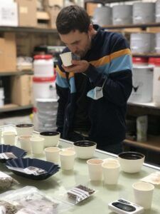Inmerso en una mesa de cafés de especialidad y abastos, una persona saborea el aroma de su taza, experimentando la esencia de una Cata de cafés de especialidad. - ForTwo - Planes para parejas